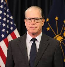 headshot of indiana gov mike braun with usa and indiana flag in background